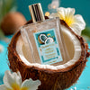 Glampton Caribbean Coconut Shimmer Fragrance Mist bottle resting inside a halved coconut, surrounded by white tropical flowers on a bright turquoise background.