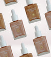 Patterned layout of Glampton Golden Hour Illuminating Drops and Endless Summer Glow Bronzing Drops bottles arranged on a light gradient background.