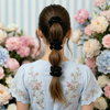 Person with a ponytail and  black scrunchies in front of a floral arrangement